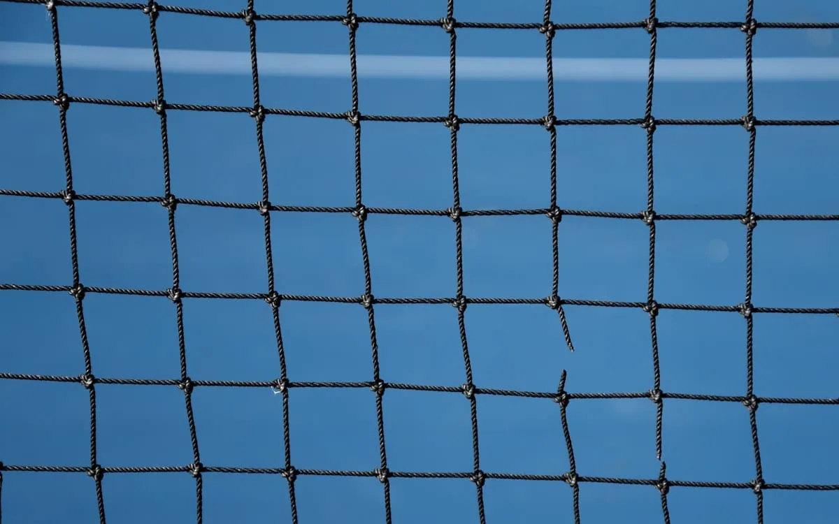 A tennis net photographed close up against a deep blue hard court, the view the ball crew have all fortnight